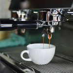 Close-up of espresso pouring from a shiny coffee machine into a white cup, perfect for lovers of caffeine and barista art.