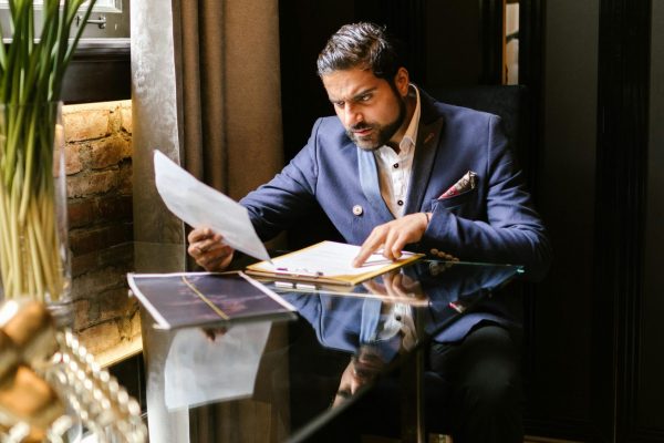 A well-dressed man in a suit reading documents at a stylish hotel lounge with elegant decor.